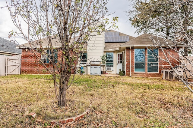 rear view of property featuring a lawn and solar panels