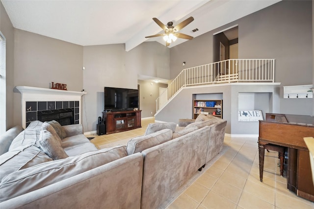 living room featuring ceiling fan, light tile patterned floors, a tiled fireplace, and vaulted ceiling with beams