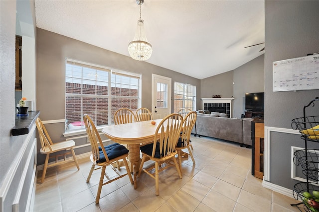 dining room featuring lofted ceiling, light tile patterned floors, a tiled fireplace, and ceiling fan with notable chandelier