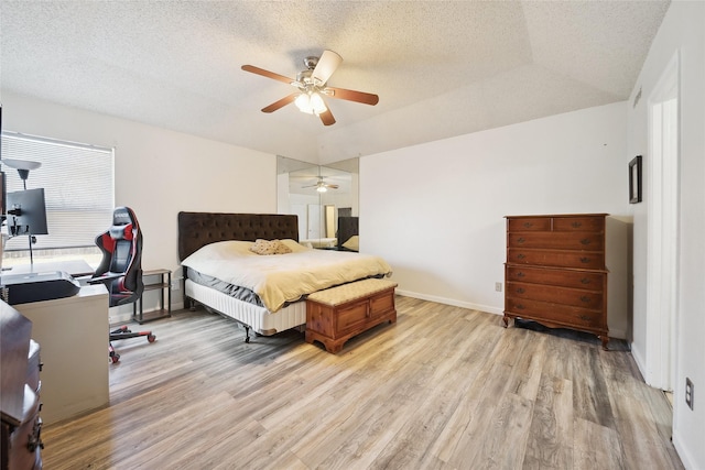 bedroom with light wood-type flooring, ceiling fan, a textured ceiling, and a raised ceiling