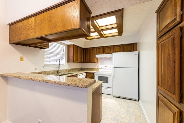 kitchen featuring kitchen peninsula, light stone countertops, sink, and white appliances