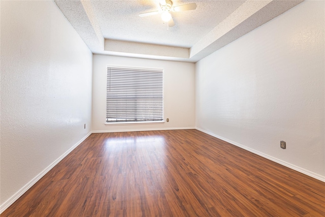 empty room featuring a textured ceiling, ceiling fan, dark hardwood / wood-style flooring, and a tray ceiling