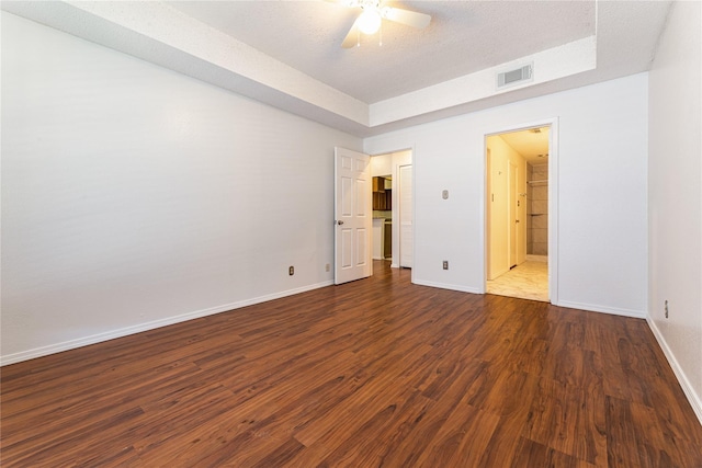 unfurnished bedroom with ceiling fan, ensuite bath, a tray ceiling, a textured ceiling, and dark hardwood / wood-style flooring