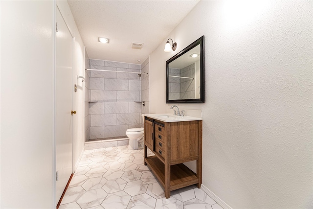 bathroom featuring toilet, a tile shower, and vanity