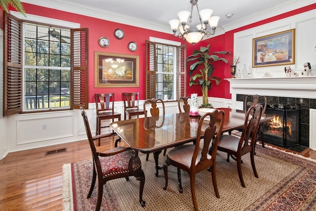 dining space with a fireplace, wood finished floors, a decorative wall, a chandelier, and ornamental molding