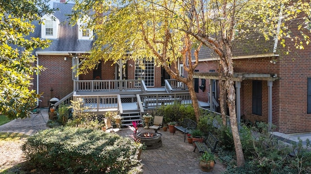 rear view of property with a fire pit, brick siding, a deck, a patio, and roof with shingles