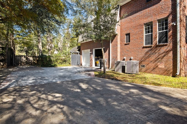 view of side of property featuring concrete driveway, brick siding, cooling unit, an attached garage, and fence