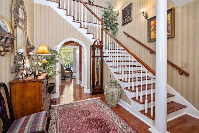 entryway featuring wallpapered walls, stairway, wood finished floors, baseboards, and arched walkways