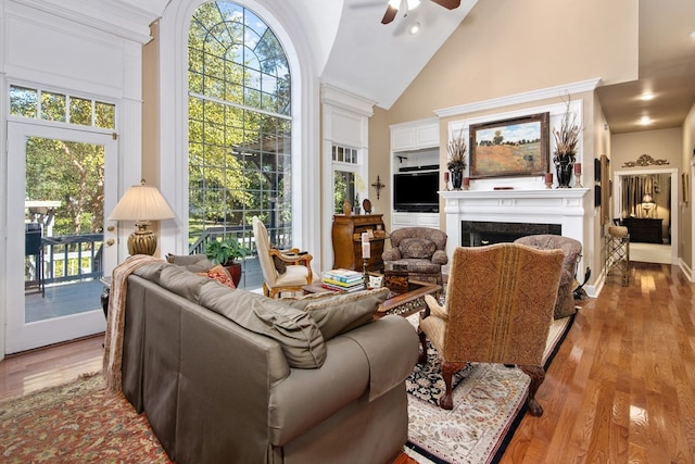 living area featuring a ceiling fan, a fireplace, light wood-style floors, high vaulted ceiling, and plenty of natural light