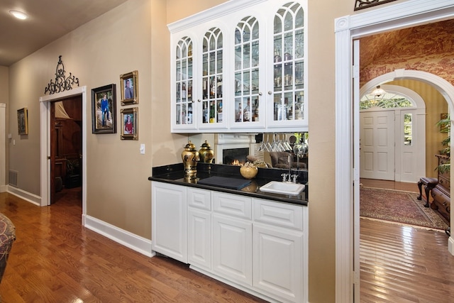 indoor wet bar with wood finished floors, baseboards, and arched walkways