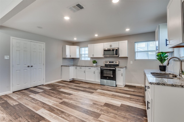 kitchen with light stone countertops, white cabinets, appliances with stainless steel finishes, and sink