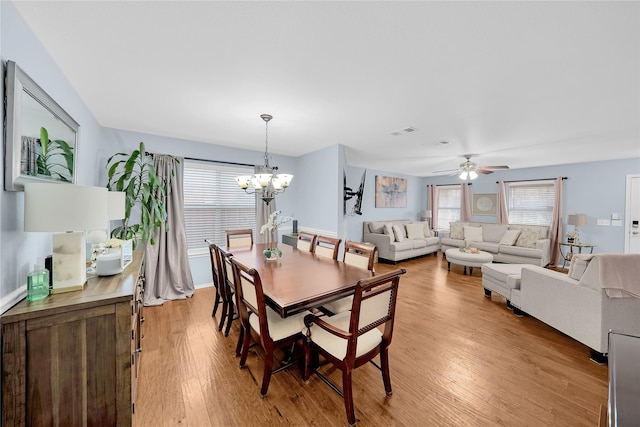 dining room with ceiling fan with notable chandelier and light hardwood / wood-style flooring