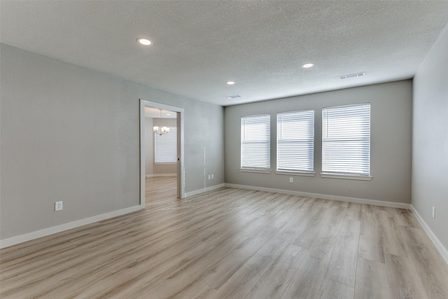 unfurnished room featuring a textured ceiling, an inviting chandelier, and light wood-type flooring