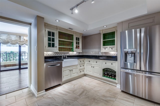 kitchen with appliances with stainless steel finishes, a raised ceiling, backsplash, light tile patterned flooring, and sink