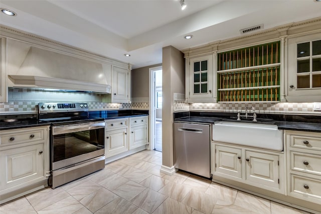 kitchen with custom exhaust hood, cream cabinetry, appliances with stainless steel finishes, decorative backsplash, and sink