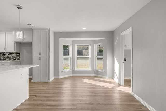 interior space featuring tasteful backsplash, decorative light fixtures, light wood-type flooring, and light stone counters