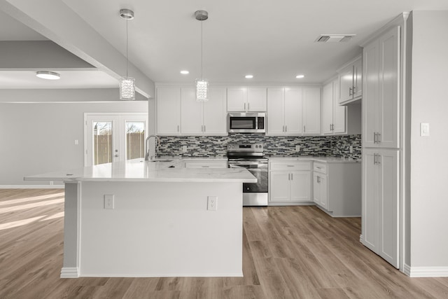 kitchen with french doors, stainless steel appliances, a center island with sink, and hanging light fixtures