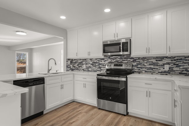 kitchen featuring light stone countertops, appliances with stainless steel finishes, white cabinetry, light hardwood / wood-style floors, and sink