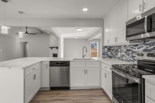 kitchen with kitchen peninsula, sink, hanging light fixtures, stainless steel appliances, and white cabinets