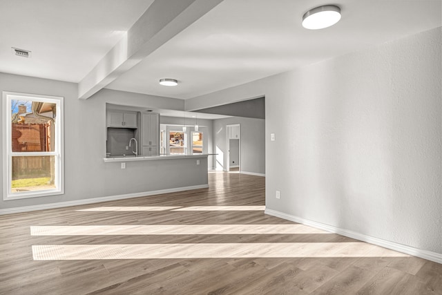 unfurnished living room featuring beam ceiling, wood-type flooring, plenty of natural light, and sink