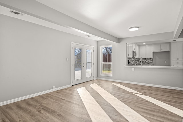 unfurnished living room featuring sink, french doors, and light wood-type flooring