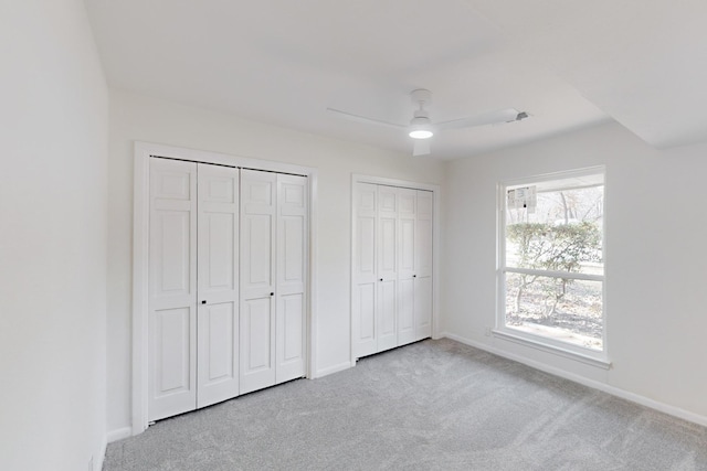 unfurnished bedroom with ceiling fan, two closets, and light colored carpet