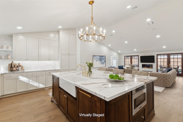 kitchen with lofted ceiling, decorative light fixtures, sink, stainless steel microwave, and light hardwood / wood-style flooring