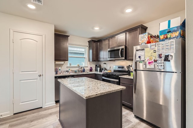 kitchen with stainless steel appliances, light wood-type flooring, light stone counters, dark brown cabinetry, and a center island