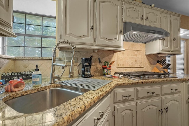 kitchen with tasteful backsplash, stainless steel gas cooktop, light stone countertops, white cabinets, and sink