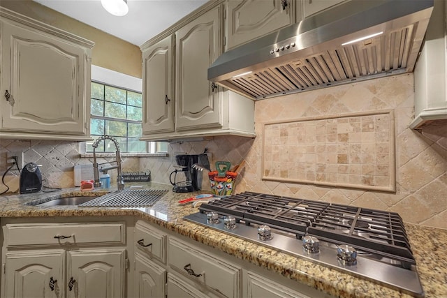 kitchen featuring light stone countertops, wall chimney exhaust hood, tasteful backsplash, sink, and stainless steel gas cooktop