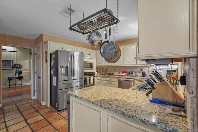 kitchen with light tile patterned floors, light stone countertops, appliances with stainless steel finishes, and kitchen peninsula