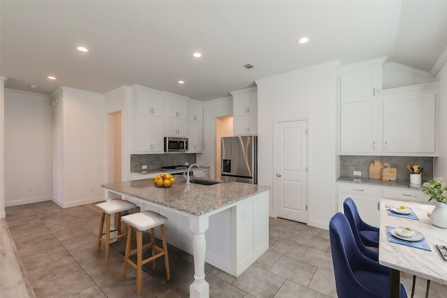 kitchen featuring white cabinets, appliances with stainless steel finishes, light stone counters, a center island with sink, and a breakfast bar area