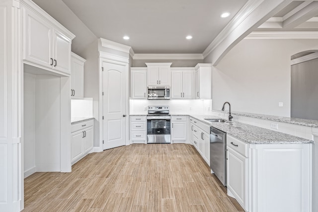 kitchen with a peninsula, white cabinets, stainless steel appliances, and a sink