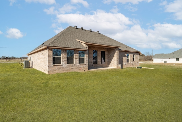 rear view of house featuring central AC unit, a lawn, a shingled roof, and brick siding