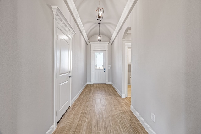 doorway to outside featuring light wood-style floors, arched walkways, vaulted ceiling, and baseboards