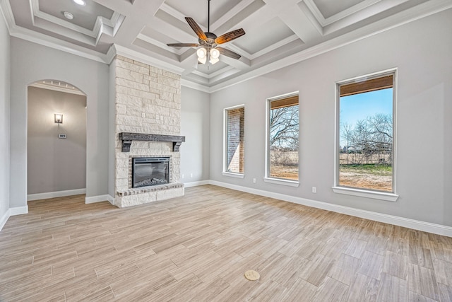 unfurnished living room with light wood-style floors, ceiling fan, a stone fireplace, and baseboards