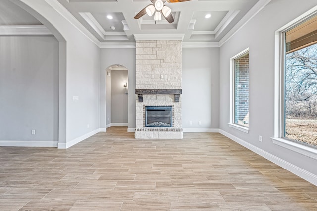 unfurnished living room featuring arched walkways, crown molding, a ceiling fan, light wood-style floors, and a stone fireplace