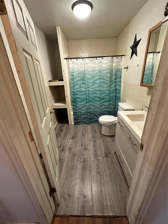 bathroom with toilet, hardwood / wood-style floors, tile walls, vanity, and curtained shower