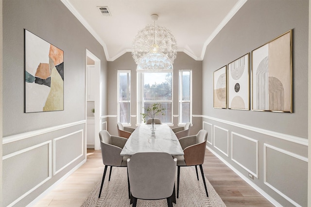 dining space with light hardwood / wood-style flooring, vaulted ceiling, ornamental molding, and a chandelier