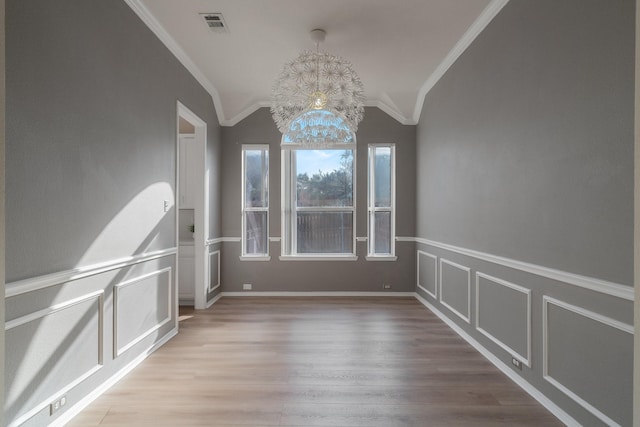 empty room featuring visible vents, wood finished floors, crown molding, a decorative wall, and lofted ceiling