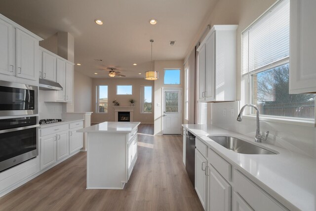 kitchen featuring stainless steel appliances, sink, light wood-type flooring, white cabinets, and a center island