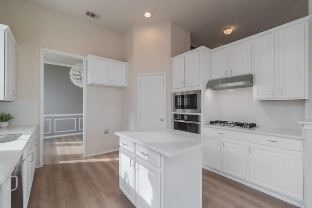 kitchen with white cabinets, dishwasher, a center island, stainless steel microwave, and light hardwood / wood-style flooring