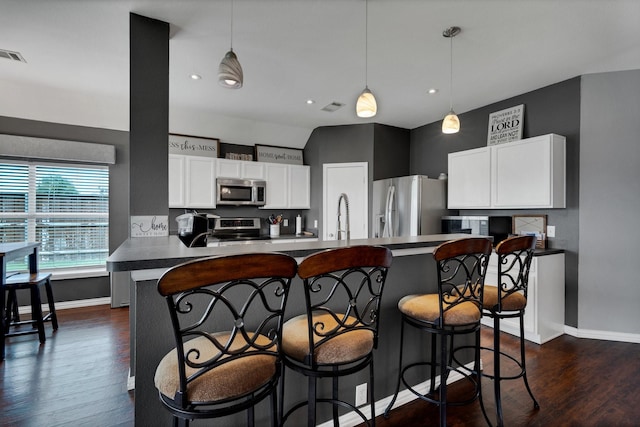 kitchen with appliances with stainless steel finishes, white cabinets, a kitchen breakfast bar, and decorative light fixtures