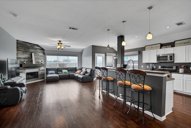 kitchen with a breakfast bar, an island with sink, hanging light fixtures, ceiling fan, and stainless steel appliances