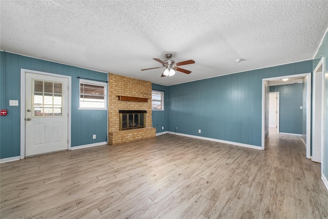 unfurnished living room with ceiling fan, a fireplace, a textured ceiling, and light hardwood / wood-style floors