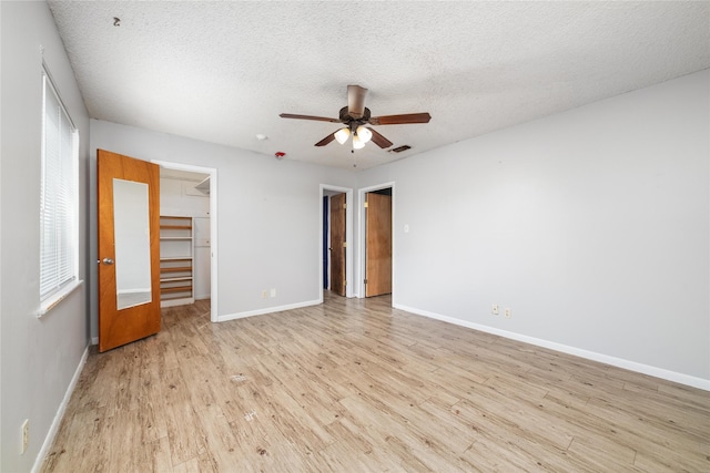 unfurnished bedroom featuring ceiling fan, light wood-type flooring, a spacious closet, a textured ceiling, and a closet