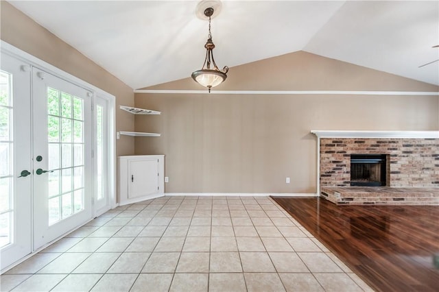 unfurnished living room with light tile patterned floors, ceiling fan, lofted ceiling, a fireplace, and french doors