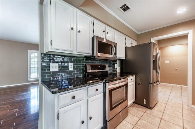 kitchen featuring light tile patterned flooring, crown molding, appliances with stainless steel finishes, white cabinets, and dark stone counters