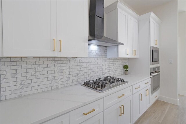 kitchen featuring appliances with stainless steel finishes, backsplash, wall chimney range hood, white cabinets, and light stone counters