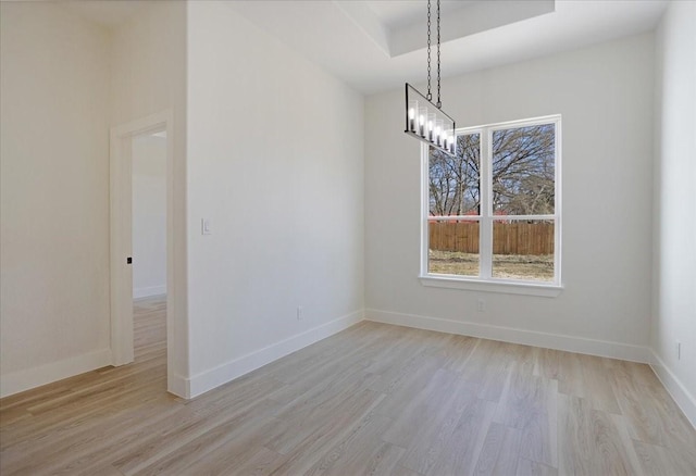 unfurnished dining area with a raised ceiling, plenty of natural light, light hardwood / wood-style floors, and a notable chandelier